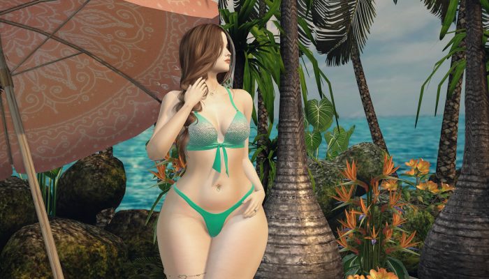 Woman standing in emerald bikini, hand in hair, ocean view behind.