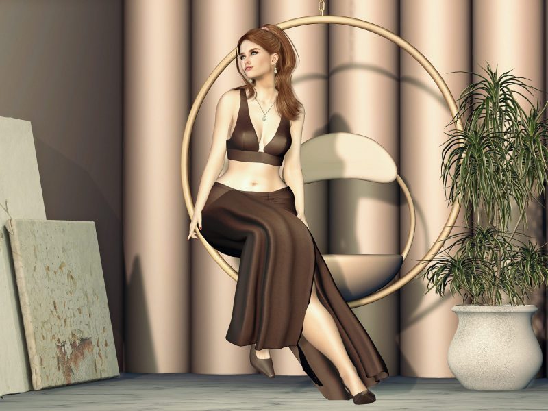 Second Life avatar in a brown crop top and flowing skirt, sitting gracefully in a round hanging chair with legs crossed.